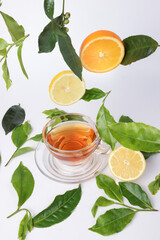 different types of fresh raw green tea leaf flower bud dropping floating elevated lemon orange slice over transparent glass teacup saucer liquid tea on white background top view