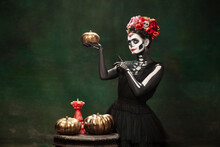 Pumpkins. Young Girl Like Santa Muerte Saint Death Or Sugar Skull With Bright Make-up. Portrait Isolated On Dark Green Studio Background With Copyspace. Celebrating Halloween Or Day Of The Dead.