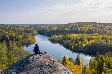 the man on top of a rock in the autumn forest on a background of a beautiful lake.