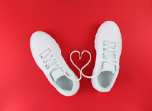 White sports shoes and heart shape from laces on a red background. Simple flat lay.