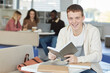 © Seventyfour - Portrait of smiling red haired boy looking at camera while studying in college library and holding textbook, copy space