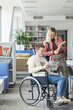 © Seventyfour - Vertical full length portrait of cheerful disabled student talking to young woman in college library