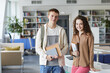 © Seventyfour - Waist up portrait of young student couple looking at camera and smiling while standing in college library holding books, copy space