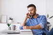 © Prostock-studio - Millennial Male Entrepreneur Talking On Cellphone And Taking Notes In Office