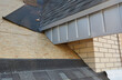 A close-up on unfinished attic roofing construction with fascia board and plywood sheathing covered with asphalt shingles using waterproofing underlayment and flashing in the roofing corners.