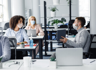 Wall Mural - Team of employees working on project and social distancing during outbreak of covid-19. Millennial male manager in protective mask talk to european and african american women