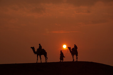 Man and a camel walking across sand dunes in Jaisalmer, Rajasthan, India.