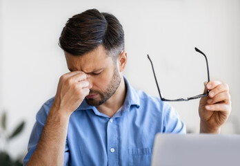 Wall Mural - Eyes Pain. Millennial businessman massaging nosebridge, tired after working on laptop computer