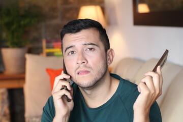 young overwhelmed man using two cellphones