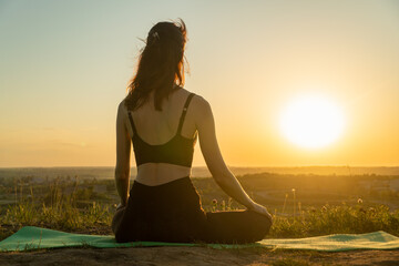 Young woman meditating in a yoga lotus pose on nature at sunset. Concept of healthy lifestyle and relaxation