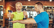 Focused mature caucasian man in sportswear doing weight exercises with assistance of a young professional personal trainer