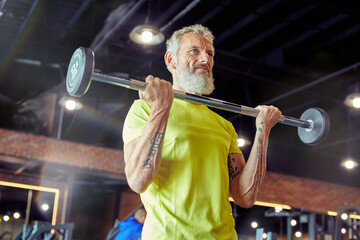 Weight workout. Strong mature man in sportswear lifting weighted bar or barbell at gym