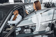 © fotofabrika - Young attractive woman salesperson in car showroom showing a car to her male client