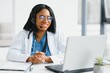 © Serhii - Smiling african american female doctor gp wears white medical coat using laptop computer at workplace gives remote online consultation, working on pc, consulting patient in internet telemedicine chat.