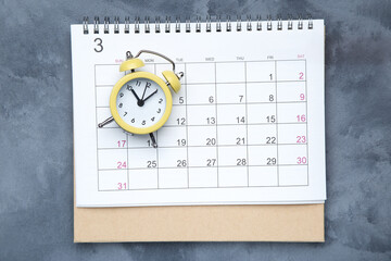 Calendar page with yellow alarm clock on grey background