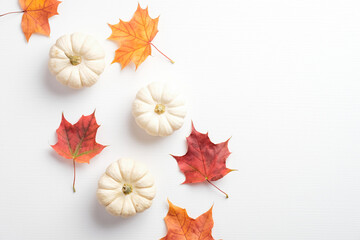 Wall Mural - Minimalist style autumn composition. Dry maple leaves and pumpkins on white background. Flat lay, top view. Autumn fall, harvest, thanksgiving concept.