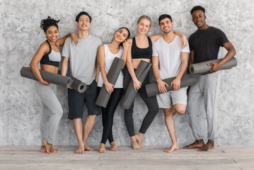 Fitness Class. Sporty multiethnic people with yoga mats posing near gray wall