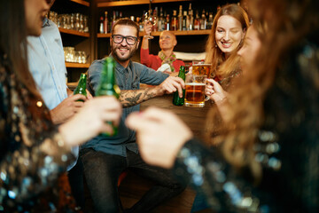 Wall Mural - Group of best friends sitting in a pub, chatting and toasting with beer.