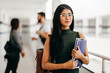 © kleberpicui - Portrait of young Brazilian student with backpack carrying books in college. Other students in the background.