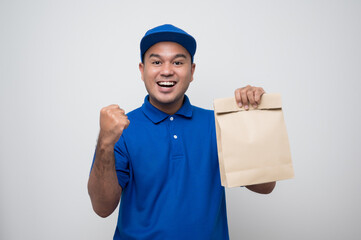 Young smiling asian delivery man in blue uniform holding paper bag food delivery on isolated white background..