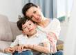 © JackF - Cheerful teen boy with his mother embracing while sitting on sofa at home..
