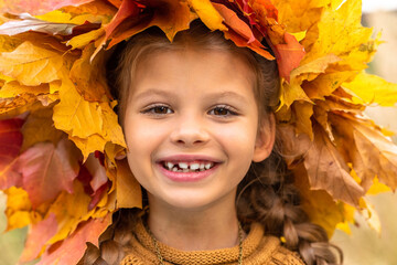 a little girl in an autumn sweater and a maple wreath.