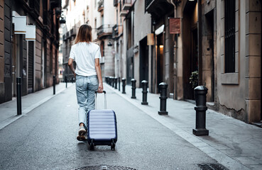 Young traveling woman with suitcase on a sunny city street. Traveler on vacation.