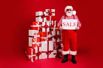 Wall Mural - Full length body size view of his he nice handsome cheerful funny bearded Santa father holding sale placard pile stack gifts delivery tradition isolated bright vivid shine vibrant red color background