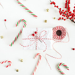 Wall Mural - Christmas gift box with festive candies, branch with red berries, reel of christmas rope on white table. Christmas, new year composition. Minimal concept. Flat lay, top view