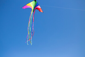 A colorful triangle kite flies under blue sky. sunny autumn.