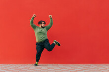 Portrait Of Funny Fat Dancer In Casual Clothes Dancing On Red Wall Background And Looking Aside At Empty Space, Isolated. A Man With Excess Weight Dances Funny Dances.