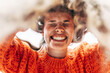 © iuricazac - Cheerful young woman smiling with white healthy teeth, wearing an orange sweater has joyful expression, posing on the sky background. Pretty female playing with her hair outdoor in the park.