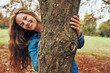 © iuricazac - Happy young woman smiling, wearing a blue denim shirt hugging a big tree, posing on nature background. Gorgeous female playing outdoor in the park.