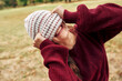 © iuricazac - Horizontal image of a gorgeous young woman wearing red sweater and hiding her eyes with a winter hat smiling broadly, posing on nature background.