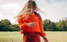 Horizontal Image Of An Young Woman With Blowing Long Blonde Hair Wearing An Orange Sweater Posing On The Sky And Nature Background. Pretty Female Playing With Her Hair Outdoor In The Park. 