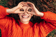 © iuricazac - Top view of a happy woman wearing orange knitted sweater doing ok gesture like binoculars, smiling broadly and looking through fingers. Pretty girl pretend to looks through binoculars at something.