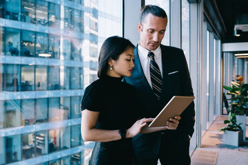 Wall Mural - Determined diverse colleagues browsing tablet in office hallway