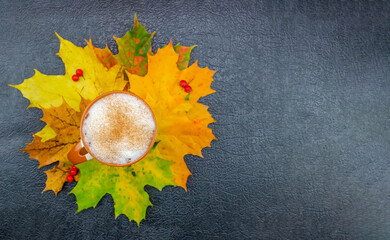 Wall Mural - Cup of cappuccino coffee stands on maple leaves on a dark background with copy space. Concept of autumn mood flat lay, family holiday, thanksgiving, home weekend. Beautiful autumn background