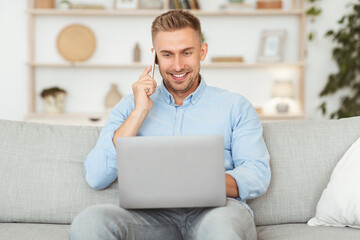 Wall Mural - Portrait of successful smiling man talking on cellphone using pc