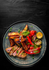 Sticker - fried meat with potatoes, pepper, tomatoes, herbs and spices in plate on black wooden table backgrou