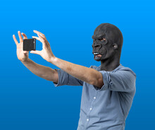 Man In Gorilla Mask Taking Selfie With Phone On Isolated Blue Background
