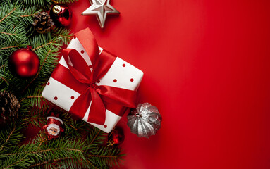 christmas composition on a red background with a white gift box, with a red ribbon with fir branches