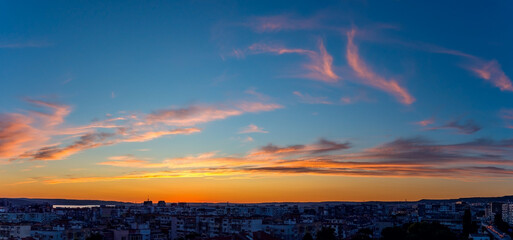 Wall Mural - panoramic shot of golden blue twilight sky with orange pink clouds over a small city. scenic skyscap