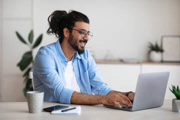 Smiling western freelancer guy working on laptop at home office