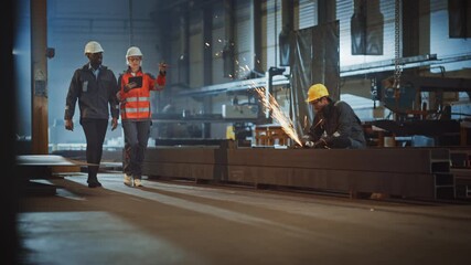 Aufkleber - Two Heavy Industry Engineers Walk in Steel Factory, Use Tablet and Discuss Work. Industrial Worker Uses Angle Grinder in the Background. Black African American Specialist Talks to Female Technician.