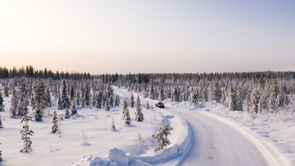 Bird’s eye view of vehicle car moving on rural road having good insurance for winter weather, aerial view of suv automobile driving in scenery area surrounded by coniferous forest.