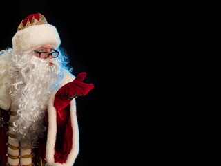 Wall Mural - Santa Claus in a red fur coat, with a white beard posing on a black background