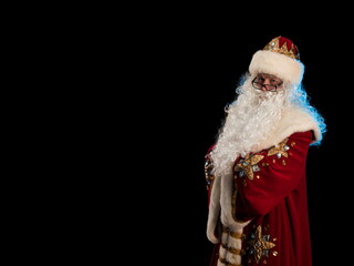 Wall Mural - Santa Claus in a red fur coat, with a white beard posing on a black background