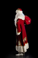 Santa Claus in a red fur coat, with a white beard posing on a black background