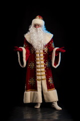 Santa Claus in a red fur coat, with a white beard and a bag of gifts posing on a black background